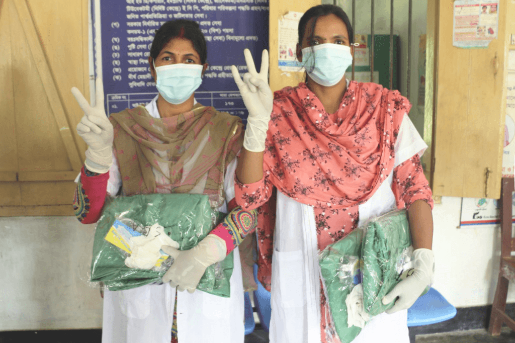 Two women wearing gloves and masks hold protective gear against COVID 19.