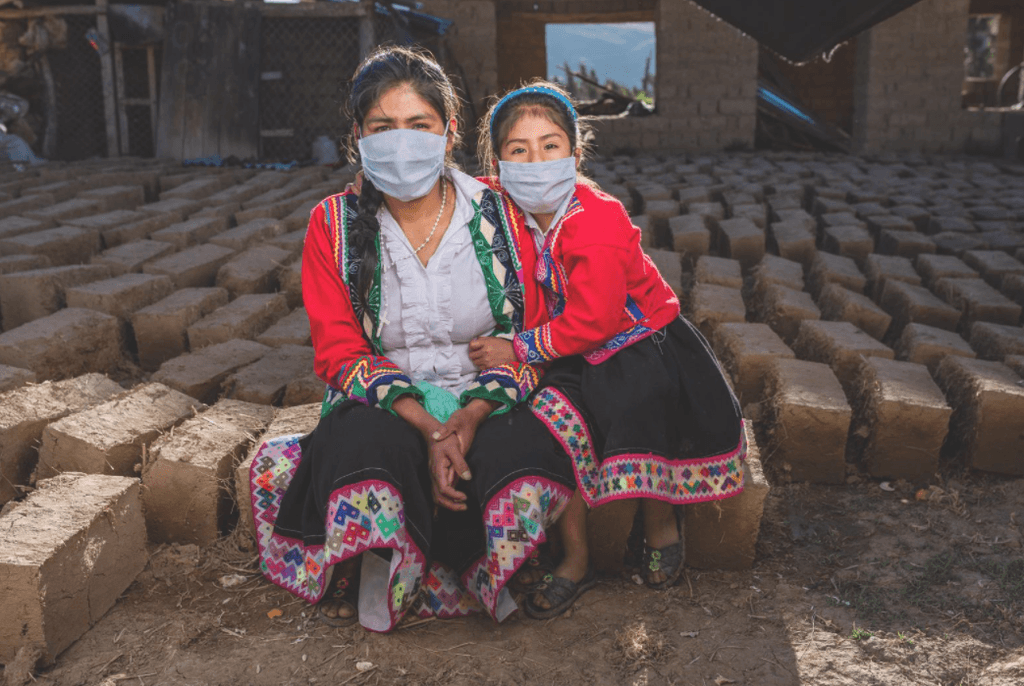 Two girls in traditional clothes sitting next to each other, wearing a mask.