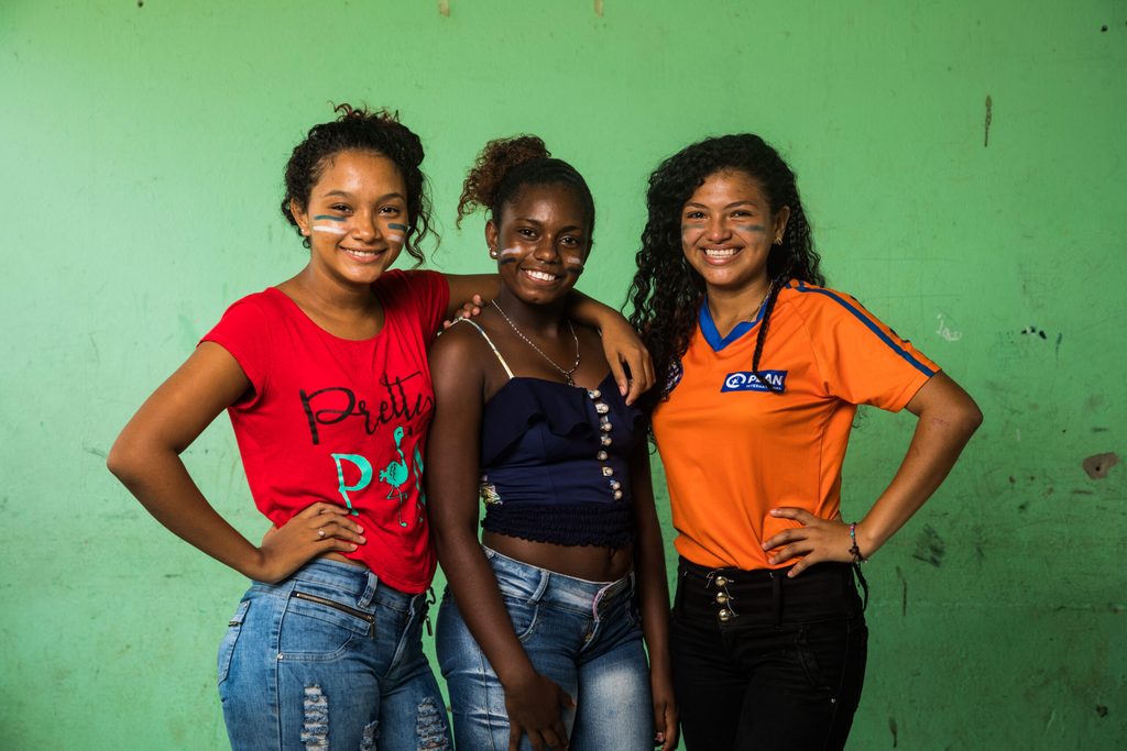 Three adolescent girls posing and smiling for the camera confidently.