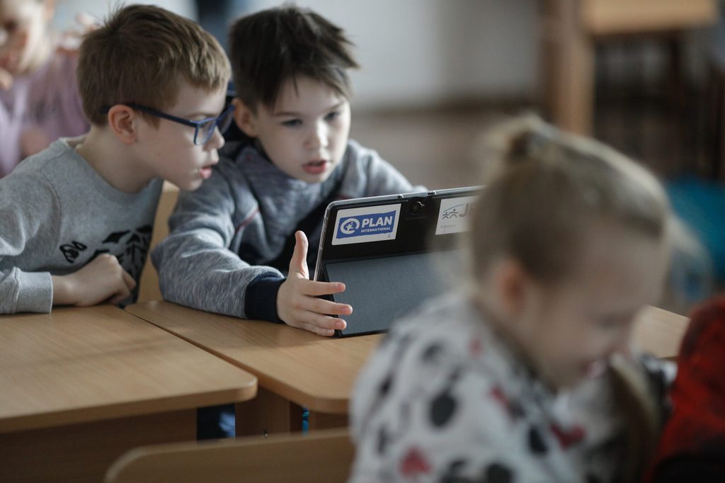 Children looking at a tablet screen during classroom in Romania.