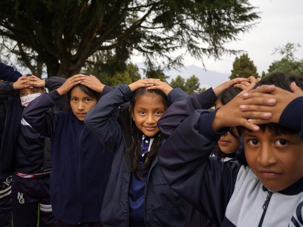 A photo of a group of children covering their heads as part of an earthquake drill, prat of the exercises that ensure they are well-prepared and knowledgeable about safety procedures.