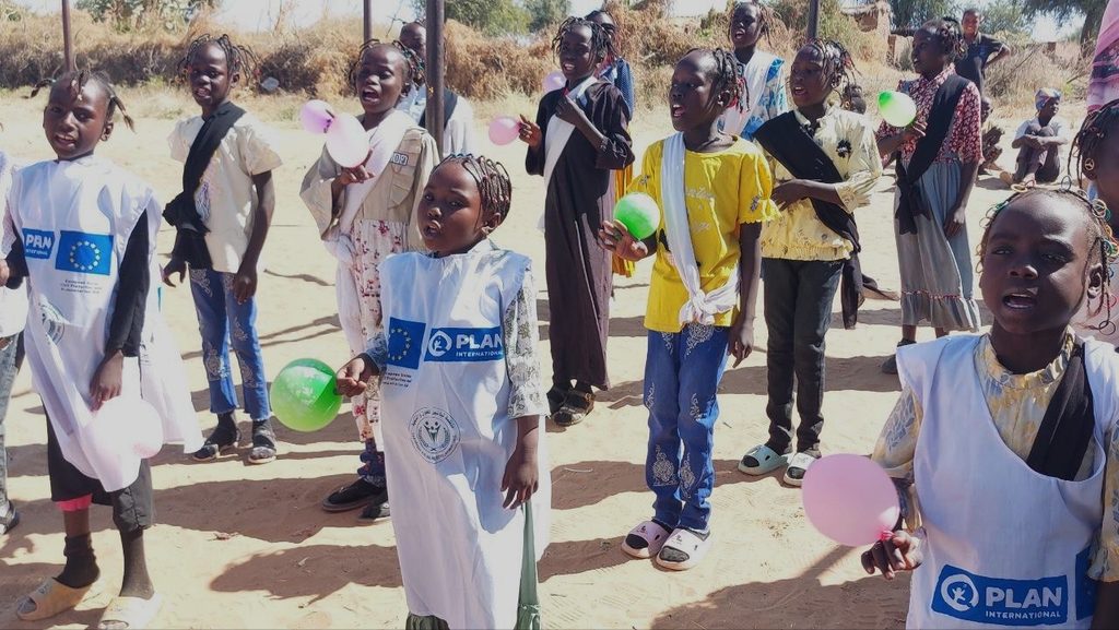 A group of children holding balloons of different colours while standing next to each other outside, on a sunny day.