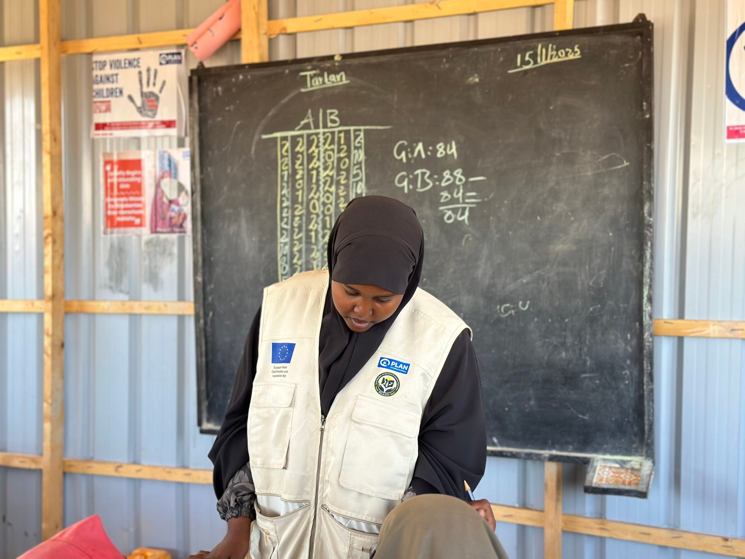 A Plan International staff member in front of a classroom's blackboard.