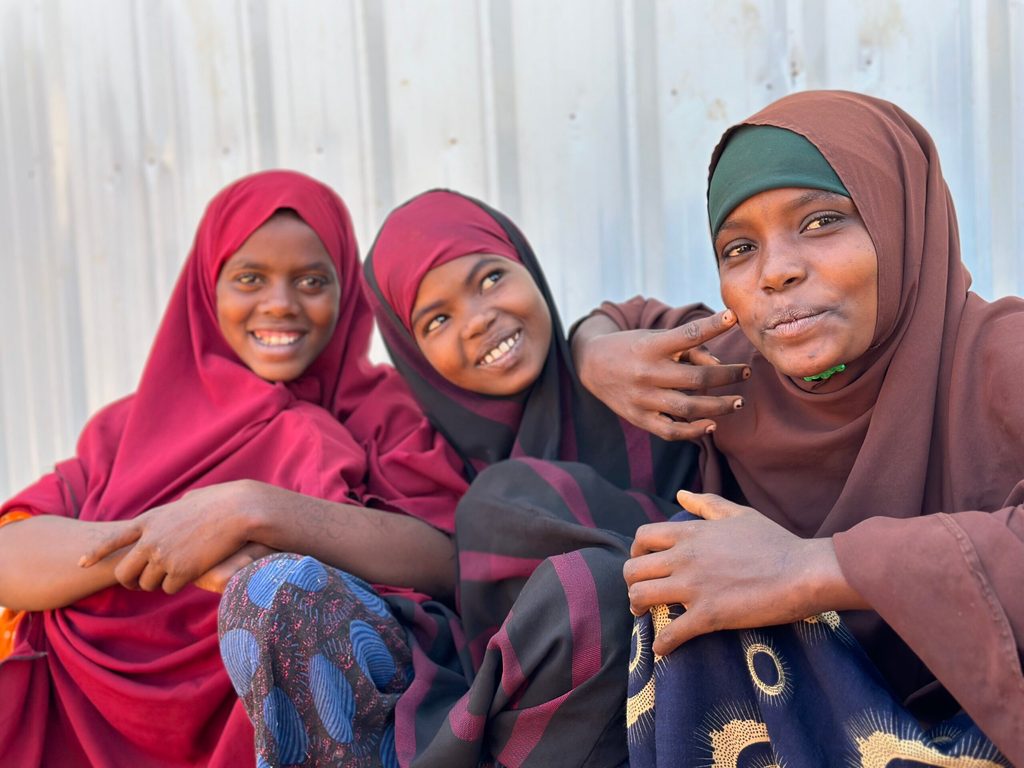Three girls posing and smiling for a photo outside their classroom in Jubaland, Somalia.
