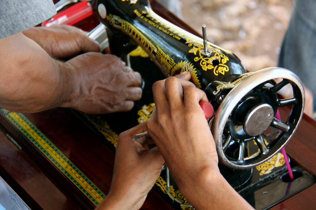 Close-up of young women’s hands repairing a sewing machine in a rural area of Timor-Leste