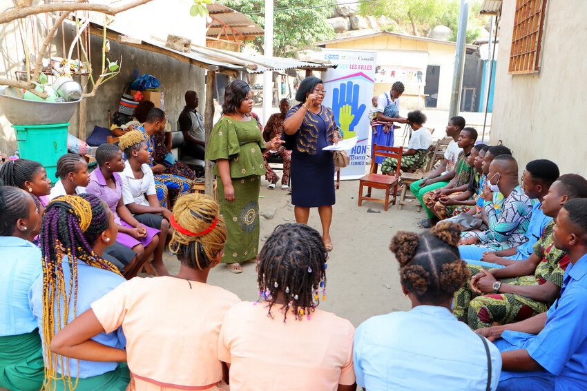 Young people sit in a circle and listen to a speaker. 