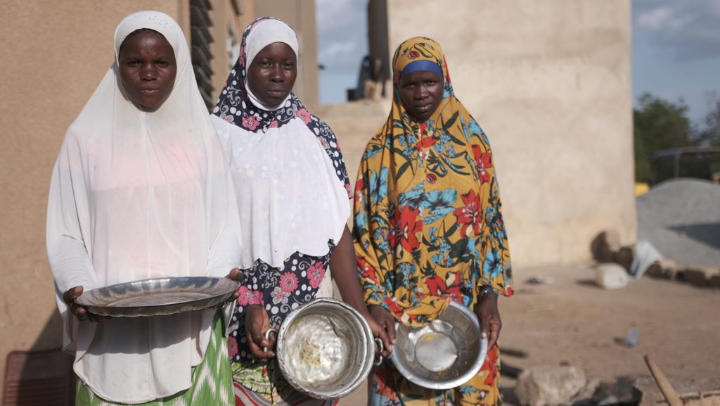 Displaced women holding empty bowls in Burkina Faso.