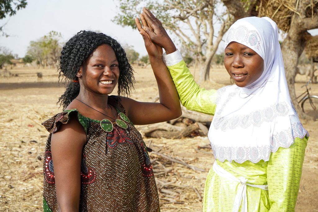 Bernadette (left) and her displaced friend Neima, both smiling and looking into the camera.