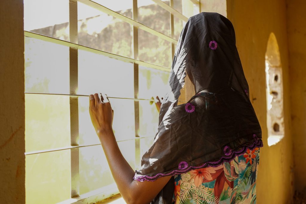 Forced marriage survivior, Saoudata*, facing away from the camera, looking out of a window.