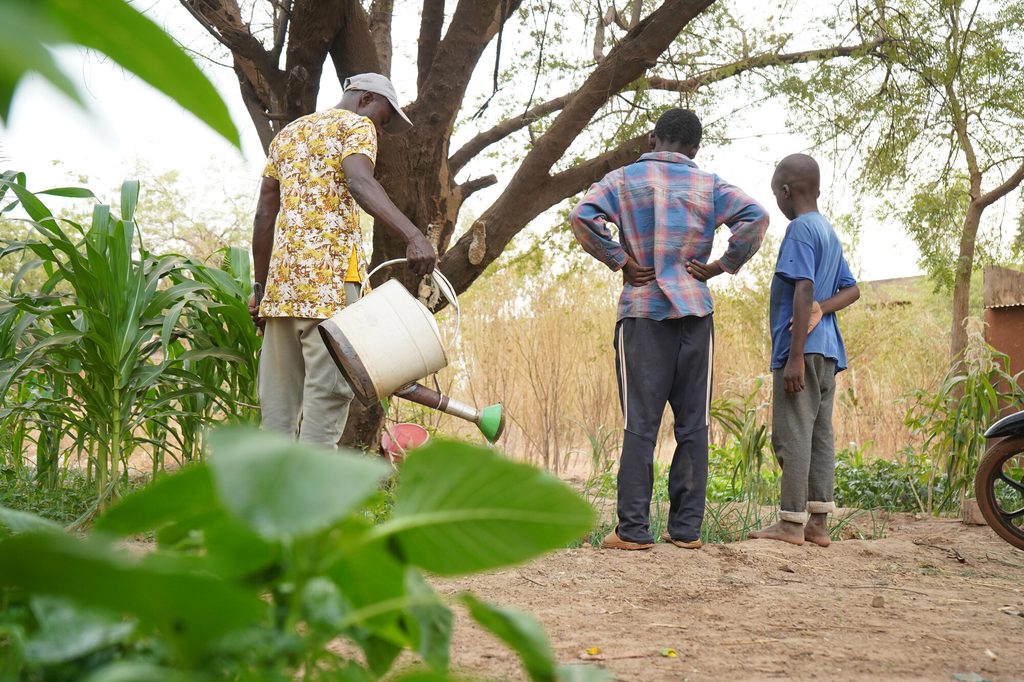Social worker Souleymane* helps Issa* and Abdou water the vegetable garden.