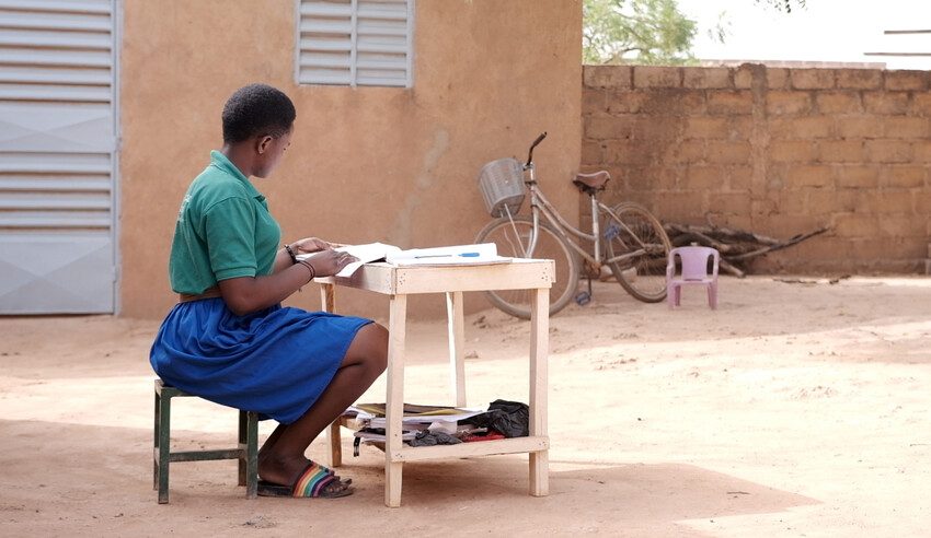 Absetou, 17, is doing her homework in her yard. She is now back in school and getting good grades.  