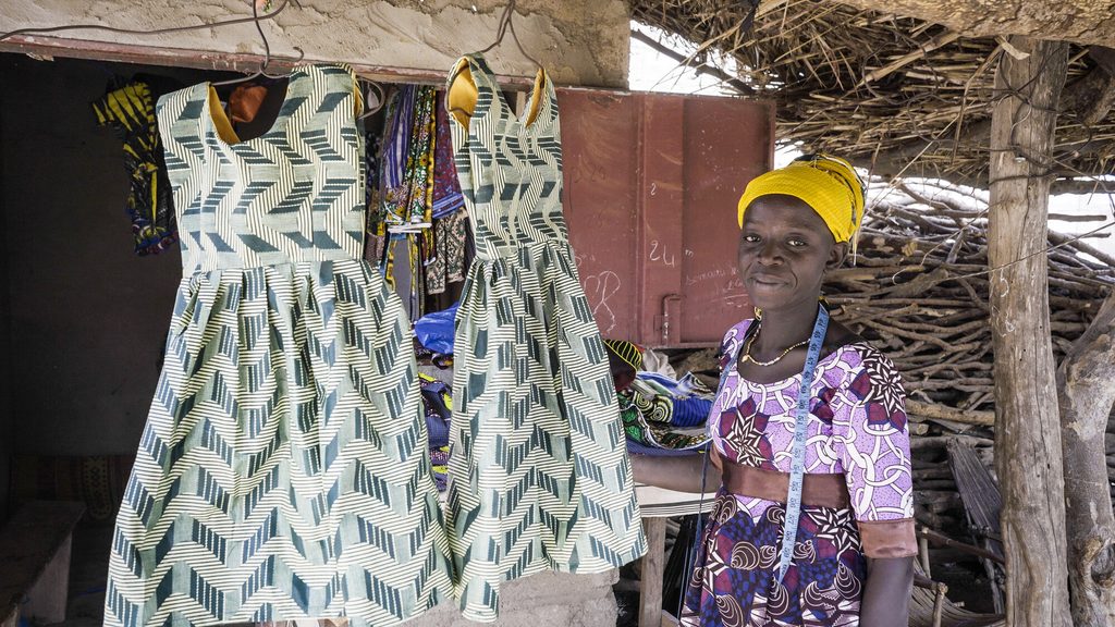 Bandiba standing next to similar dresses sewn for twin girls. 