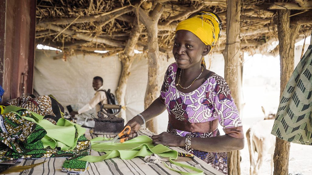 Seamstress Bandiba cuts a piece of cloth in her sewing workshop and smiles.