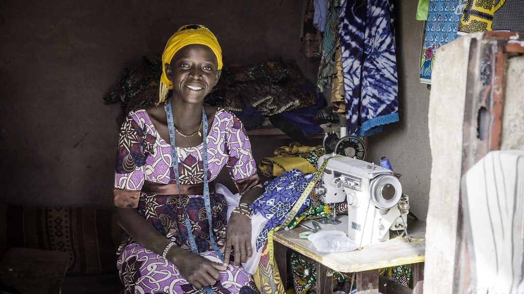 Bandiba sits next to her sewing machine and smiles. 
