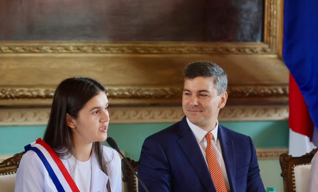 Adriana speaking into a microphone and sitting next to the President.