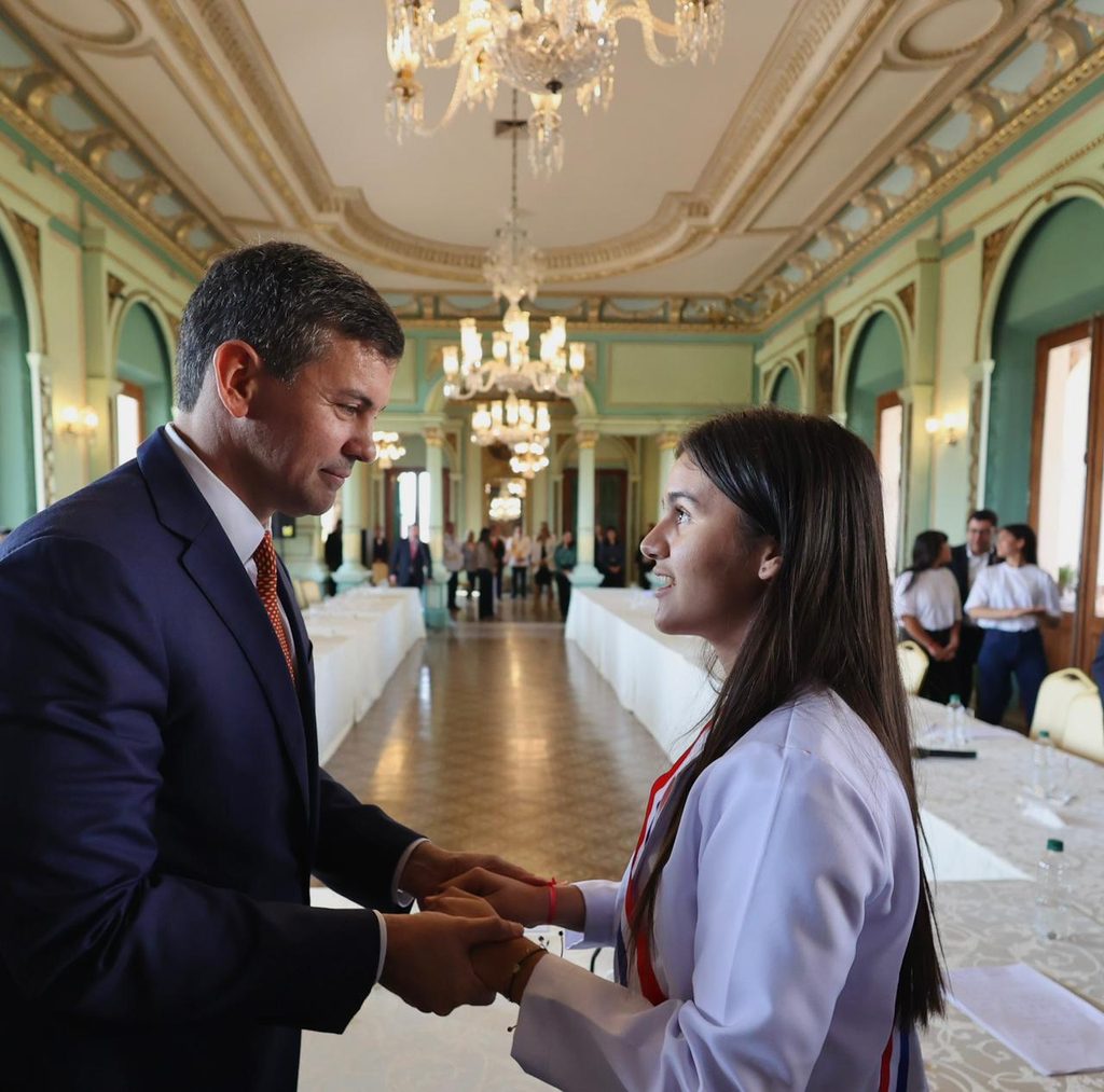 Adriana and President Pena are facing each other and touching hands as a symbol of the presidency handover. 