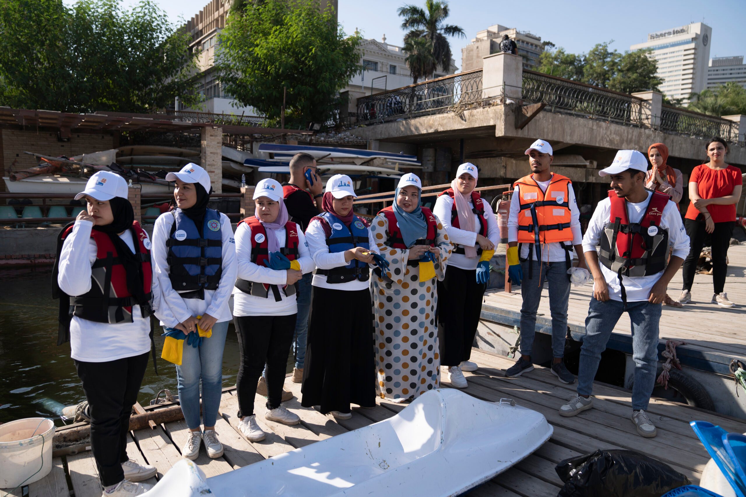 Young people stand together wearing life-jackets as they prepare for a Nile cleaning initiative.