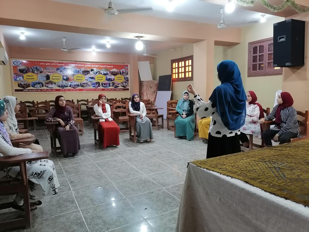 Girls sit in a circle on chairs.