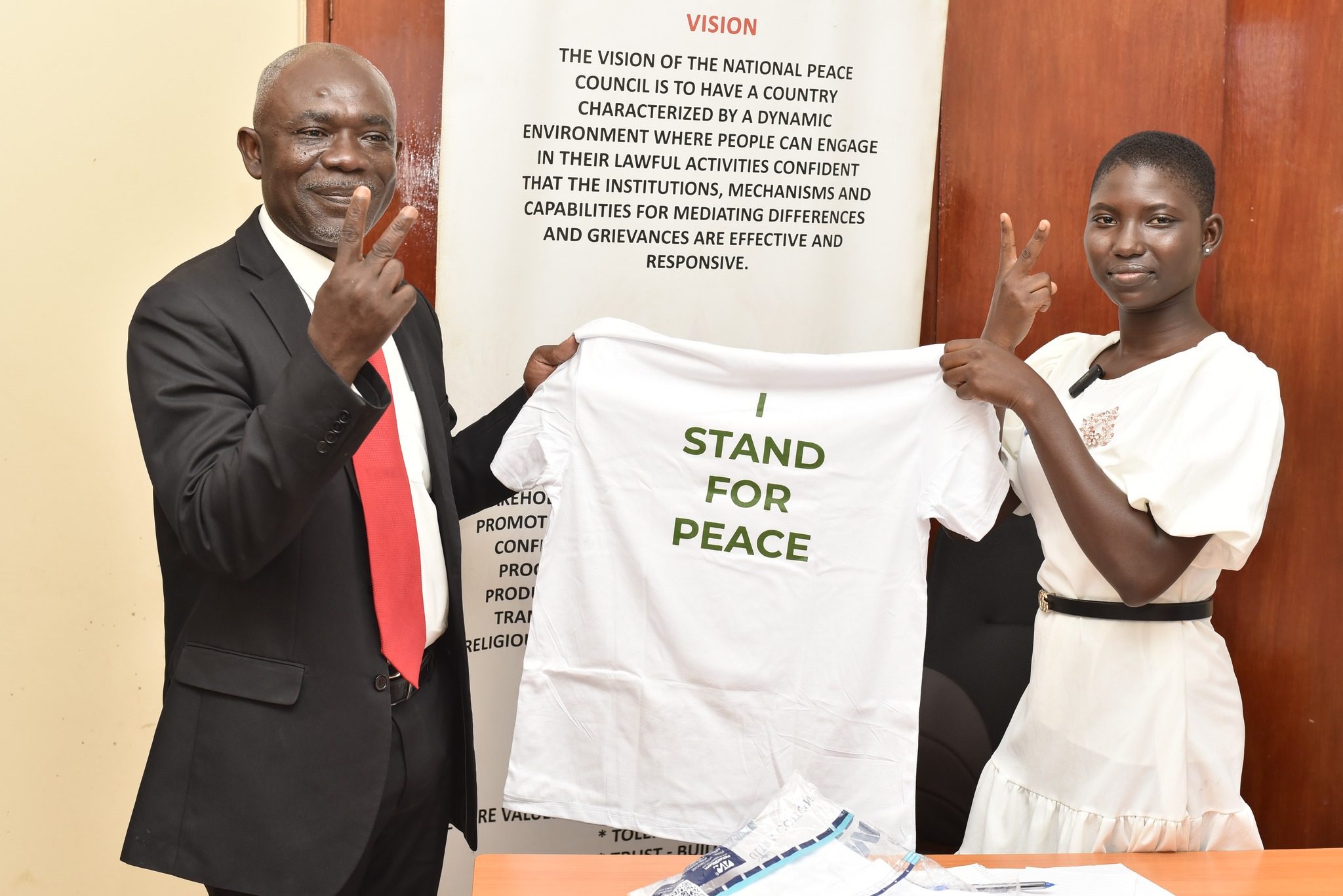 Sophia and the Board Chair of the National Peace Council hold up a peace t-shirt. 