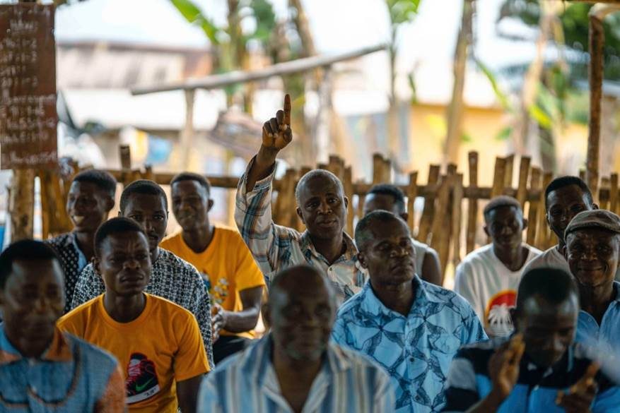 Men in the audience at a father's club meeting raise their hands to ask questions, 