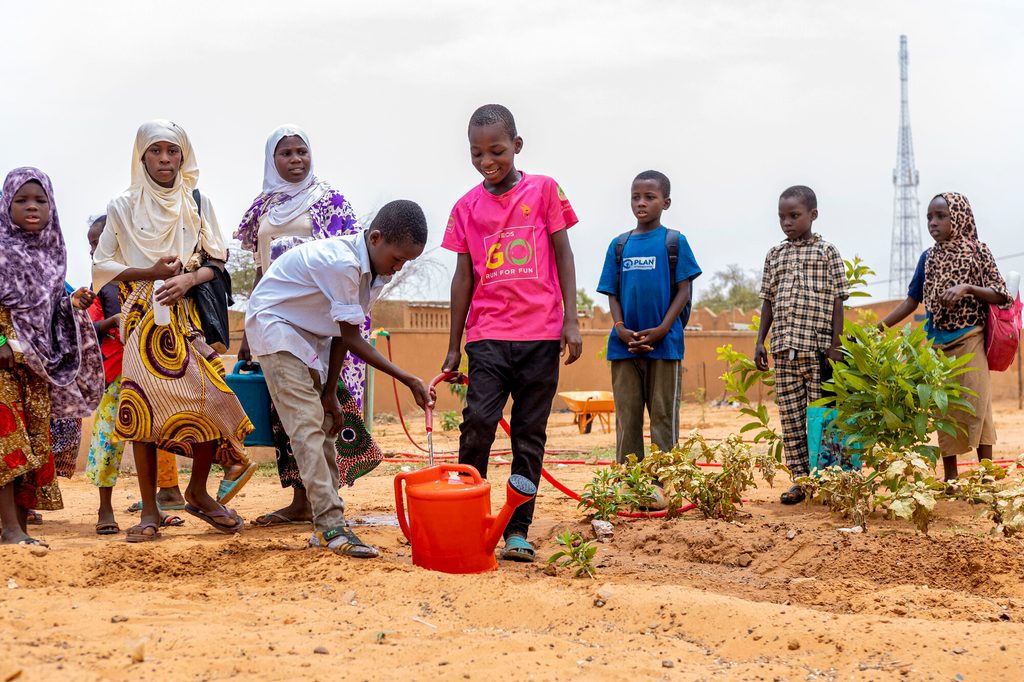 Children filling a watering can with water in a school garden in Tillaberi, Burkina Faso