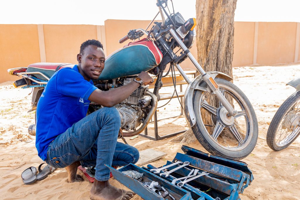 Lawali with a box of tools, repairing a motorcycle