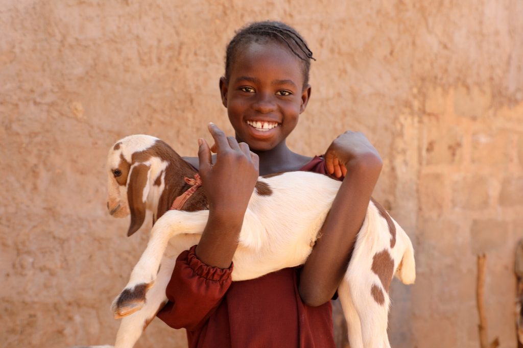 Ainee holding a young goat, smiling. 
