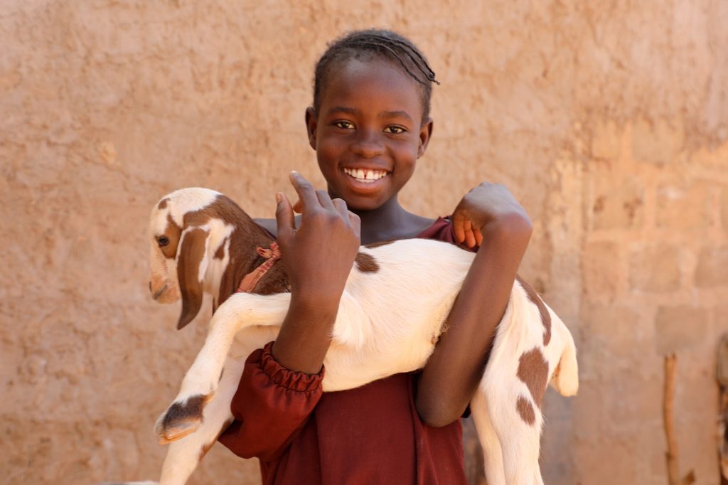Ainee holding a young goat, smiling.