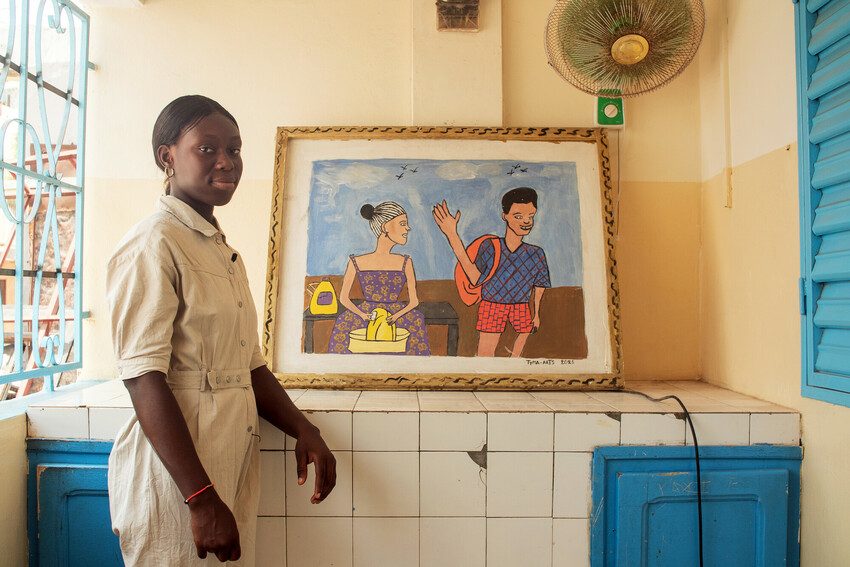 Fatoumata stands to the right of one of her paintings.