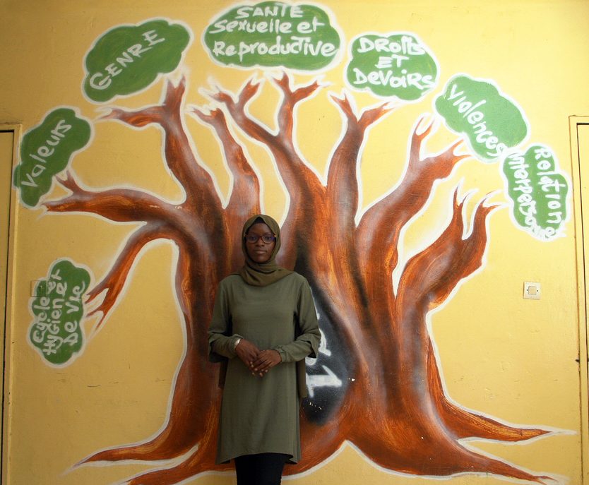 Awa standing in front of the tree mural depicting the values of the Sisters Create centre. 