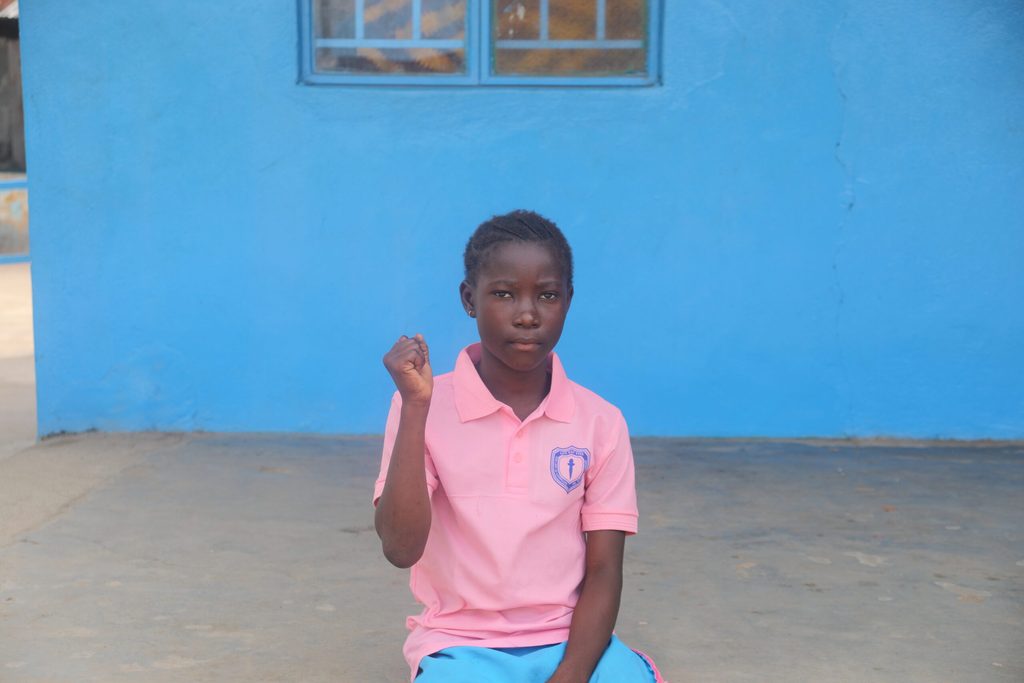 Kadiatu outside her school where she receives food through the school feeding programme implemented by Plan International