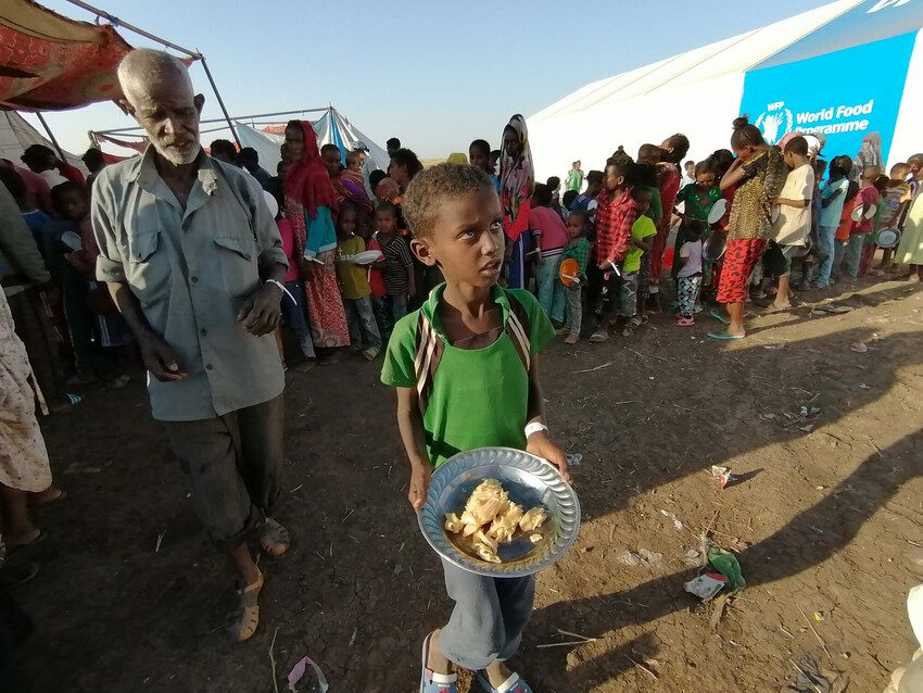 Boy collects food at border reception centre in Kassala state