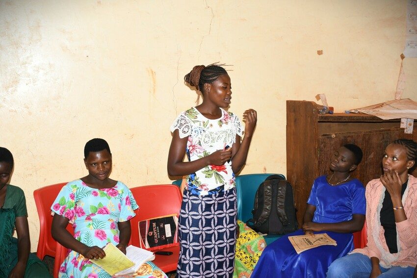 Leah standing up to speak at a meeting with other girls sitting around her.