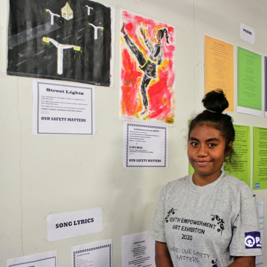 Anisa stands next to her paining at art exhibition 
