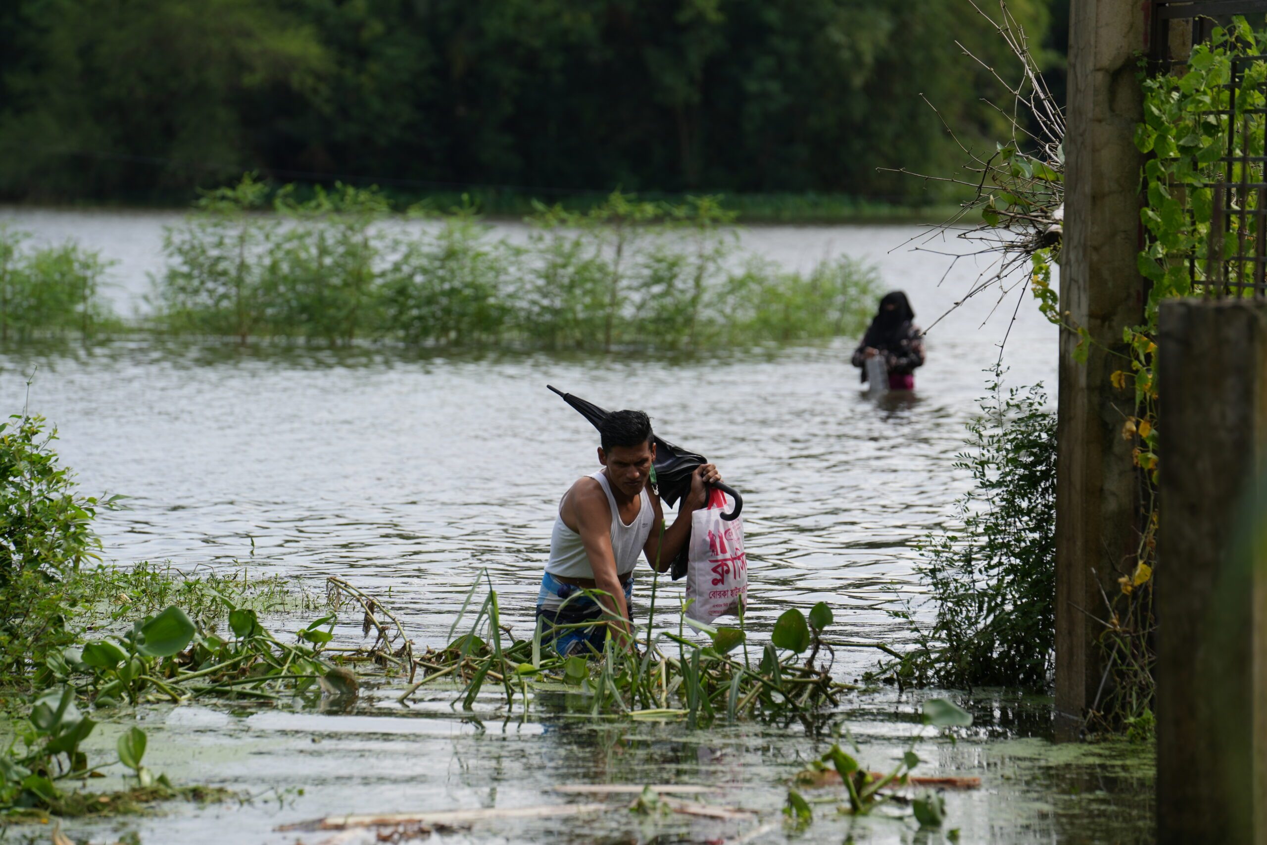 Man treading through waterlogged area with a bag and an umbrella.