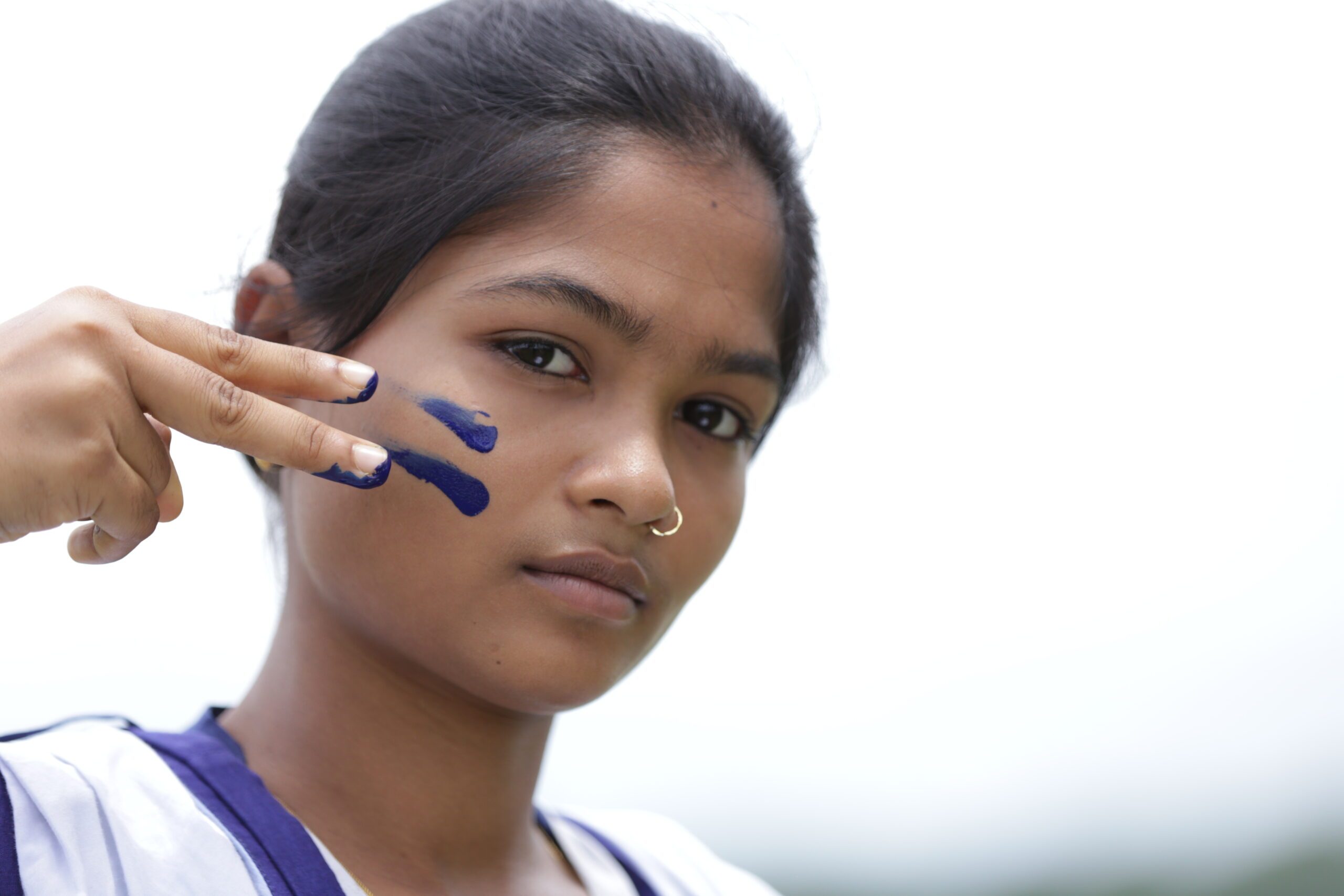 Girl with face painted with an equal sign, holding two fingers over her face representing an equal sign.