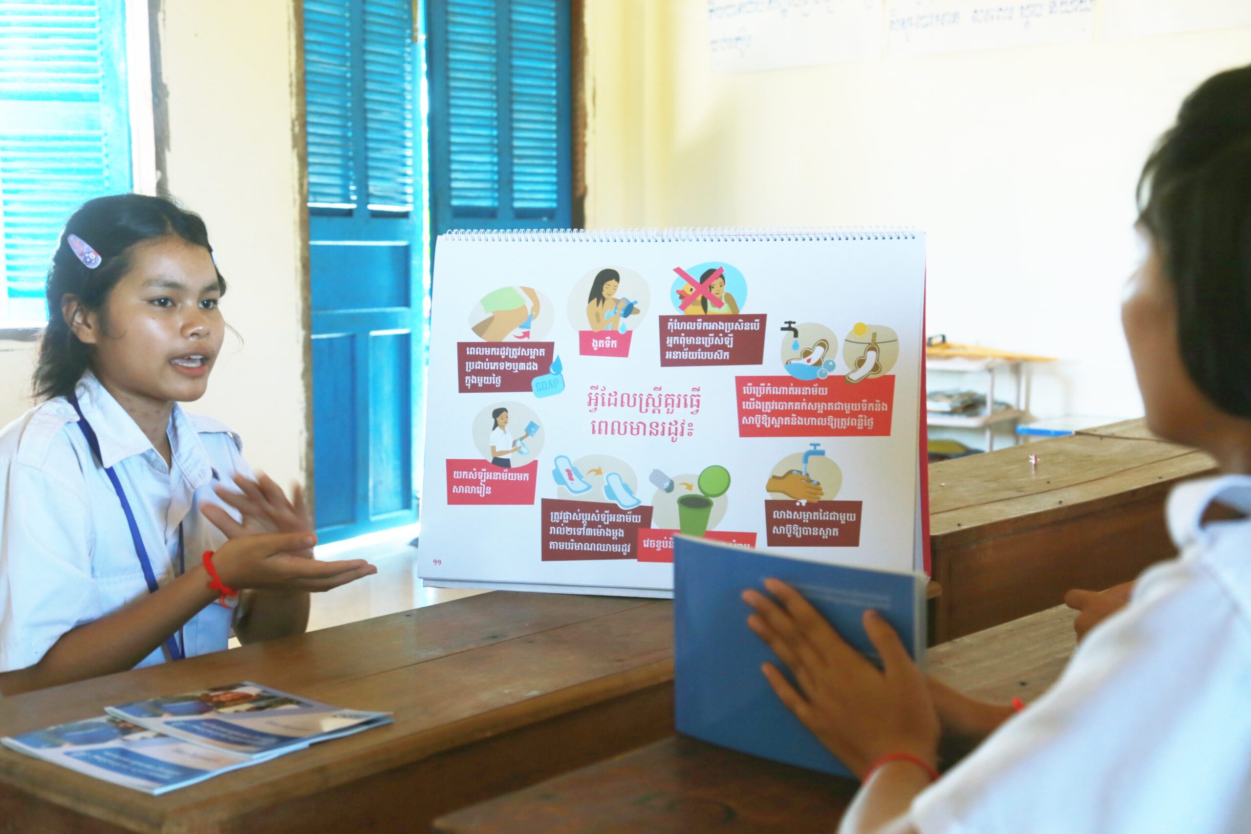 Sreyneth and a classmate sit across from each other and Sreyneth is explaining a booklet on SRHR.