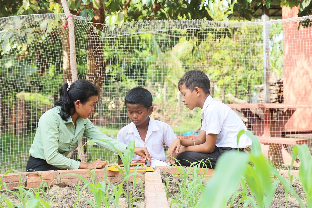 Keo is showing her students to measure the plant in the school garden.