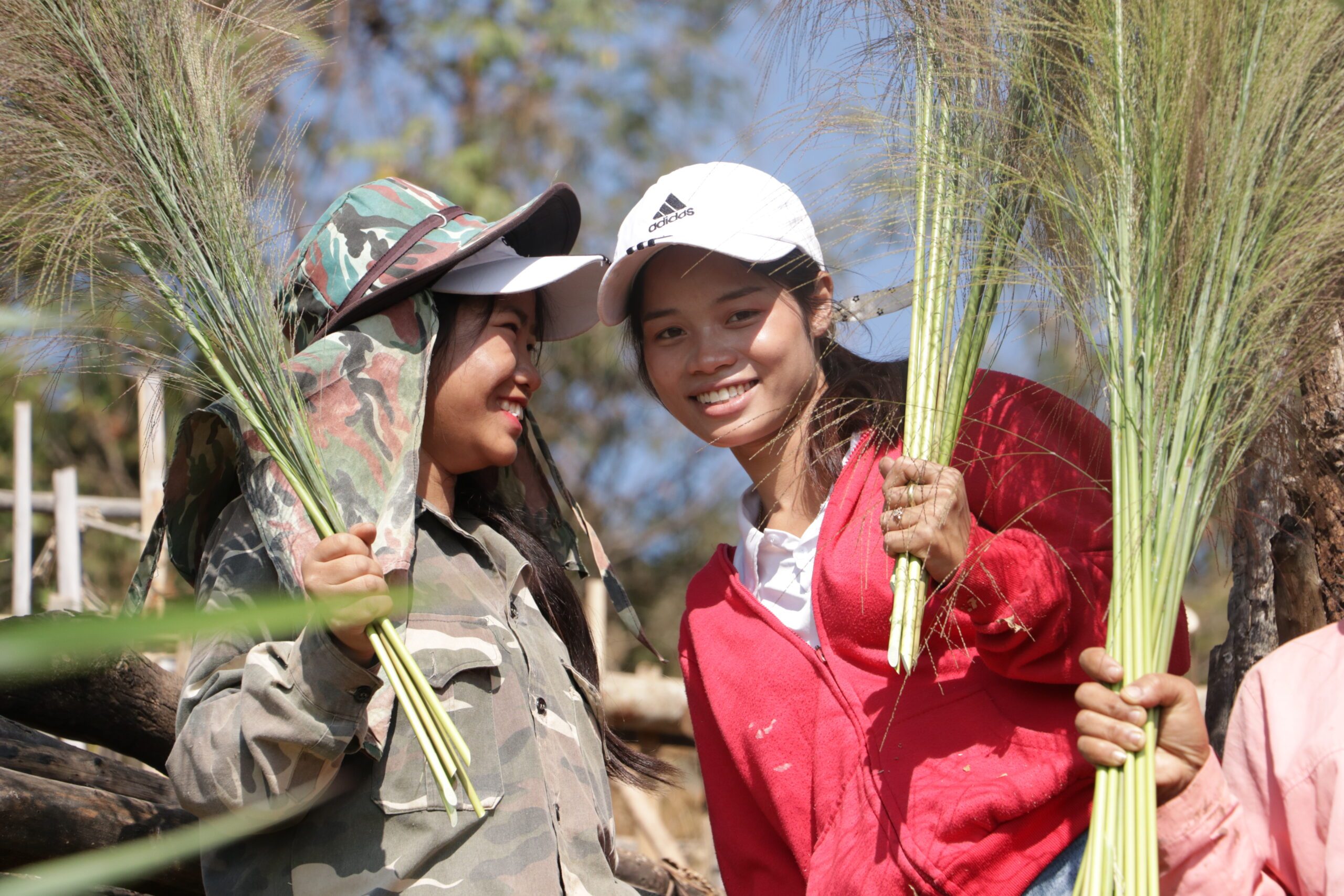 Two girls holding broom grass flowers.