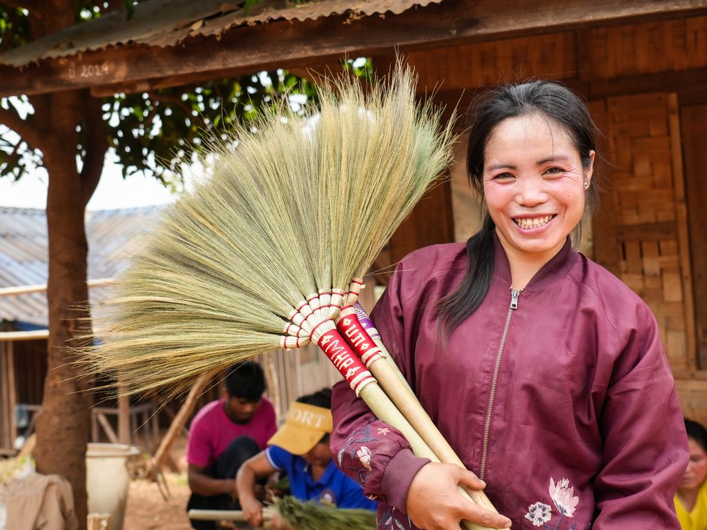 image of Jan holds brooms that are made of flowers of broom grass and she sells them to the visitors Jan holding brooms she made.