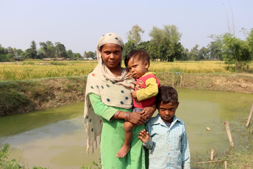 Sita, 21, and her sons in front of their fish pond