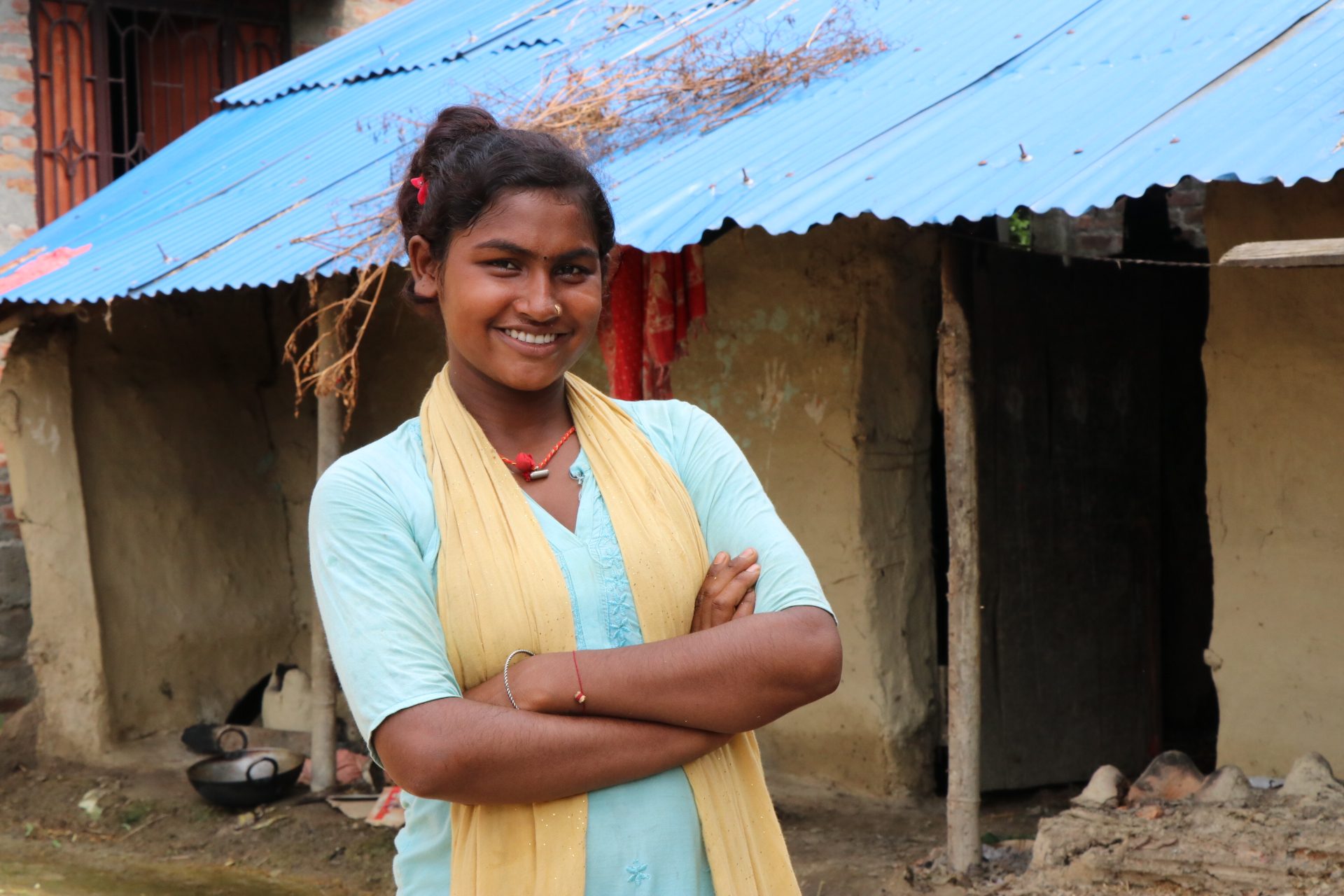 Prativa standing in front of her house with her arms folded, smiling.