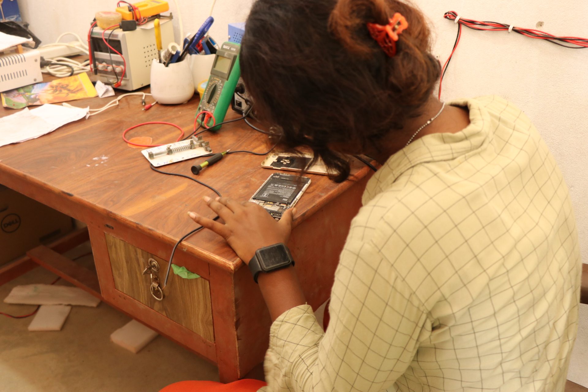 Anjali leans over the desk while repairing a phone. 