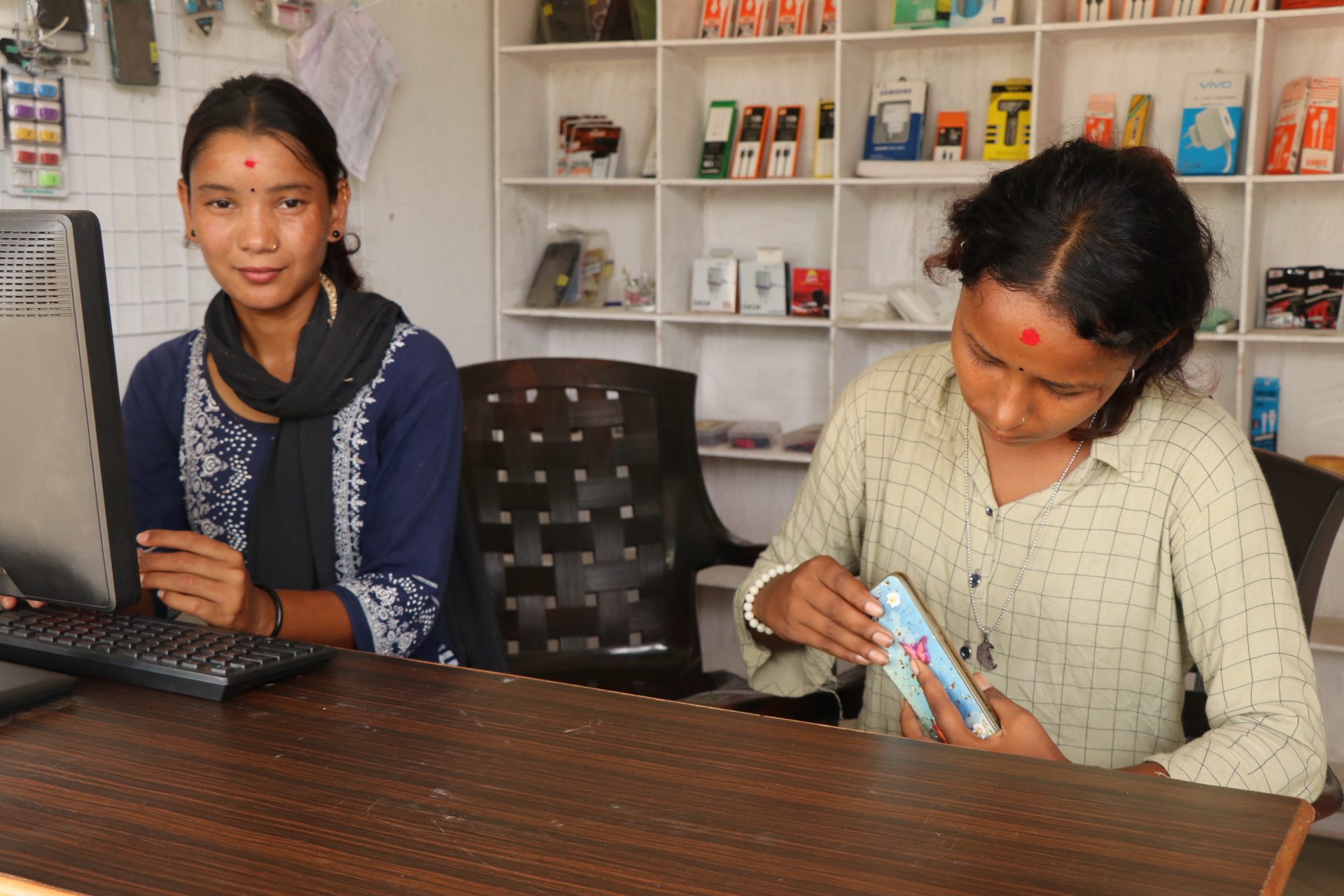 Ashmita and Anjali sitting at the desk in their mobile repair center. 