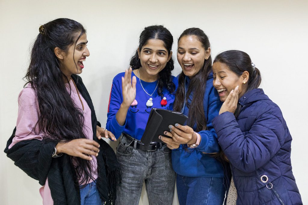Four girls are holding a mobile phone and laughing.