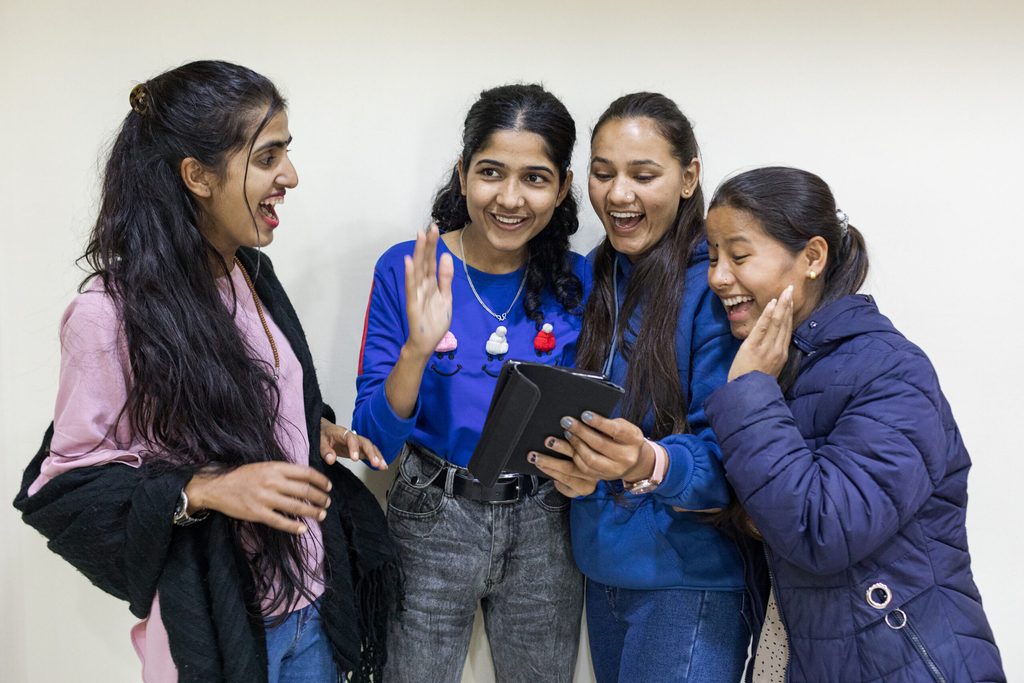 Four girls are holding a mobile phone and laughing. 
