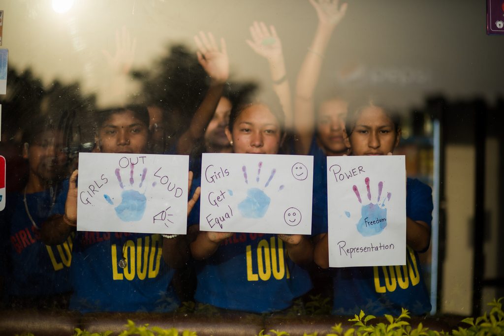 Three girls posing behind a glass wall and showing their arts.