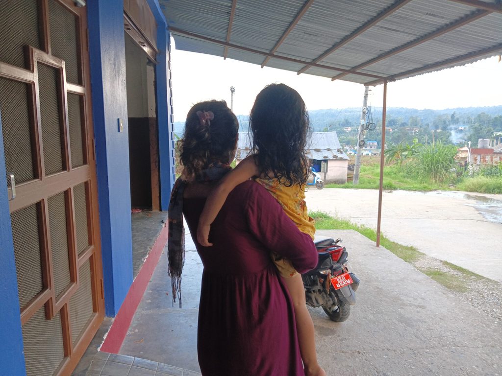Sajiya carrying her daughter outside of her home.