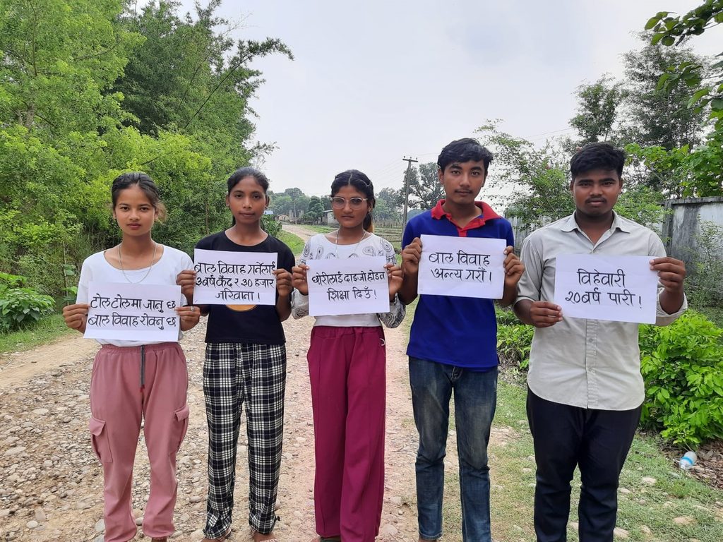 Saruna stands with four members of the adolescent girls club, holding up signs.