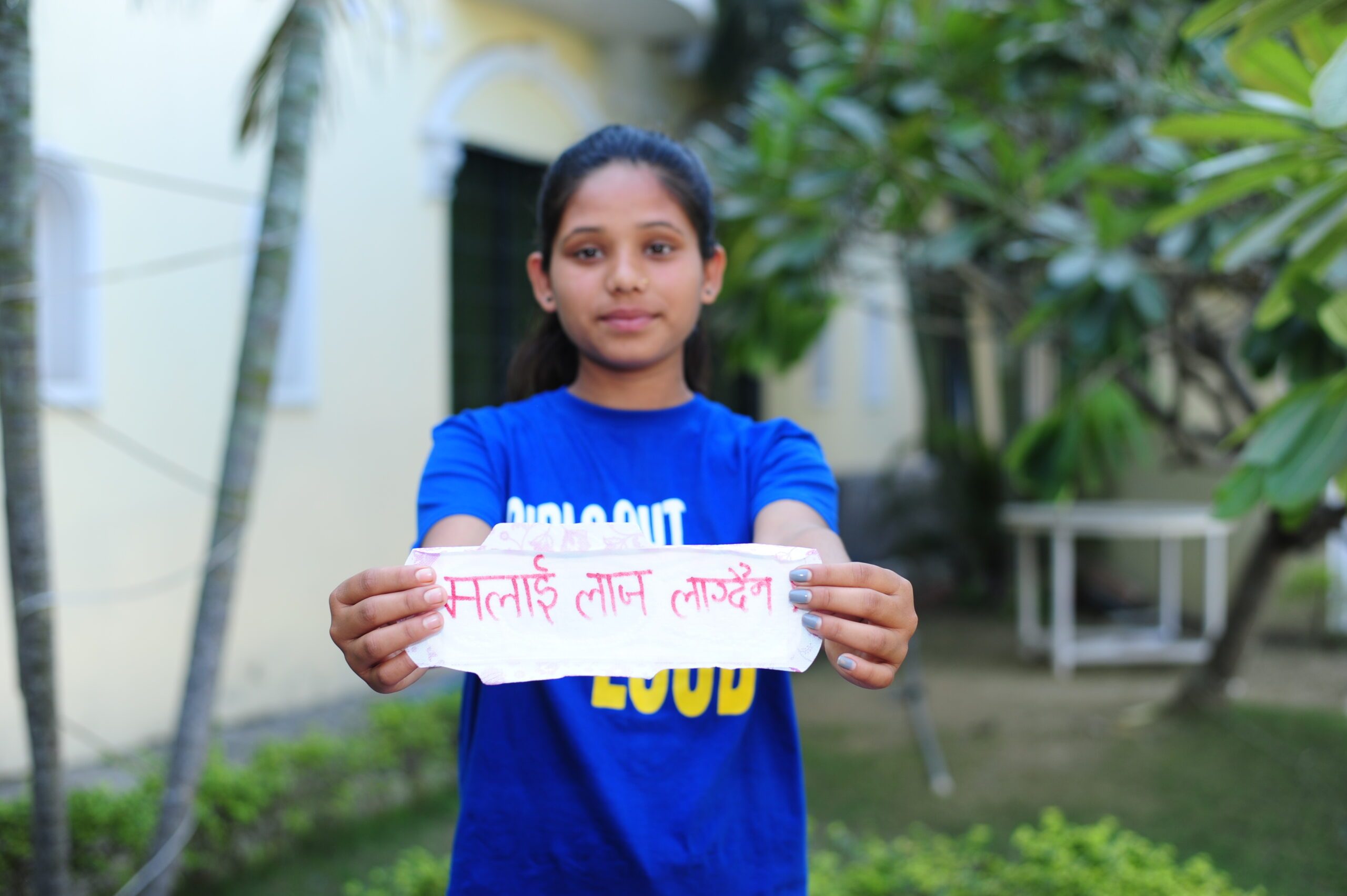 Usha holding a sanitary pad which says "I do not feel shy."